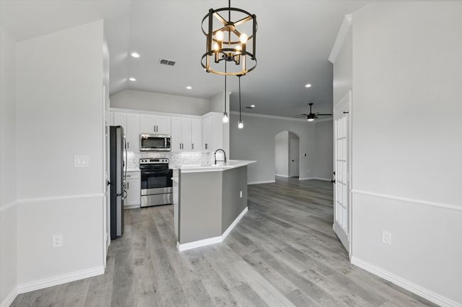 Kitchen featuring appliances with stainless steel finishes, arched walkways, open floor plan, white cabinets, and decorative backsplash | Image 10