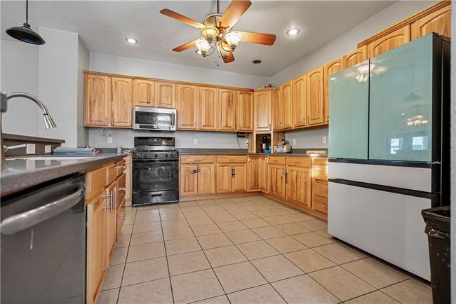 Kitchen featuring light tile patterned flooring, sink, decorative light fixtures, ceiling fan, and stainless steel appliances | Image 16