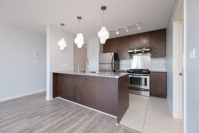 Kitchen with dark brown cabinetry, a sink, a peninsula, under cabinet range hood, and stainless steel appliances | Image 4