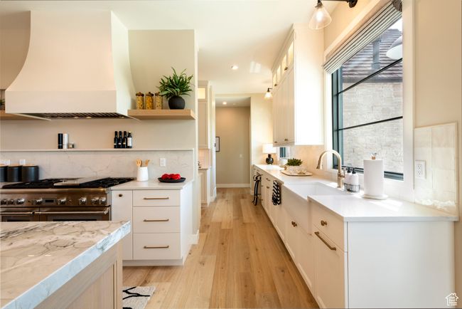 Kitchen with double oven range, custom range hood, light wood-type flooring, white cabinetry, and tasteful backsplash | Image 19