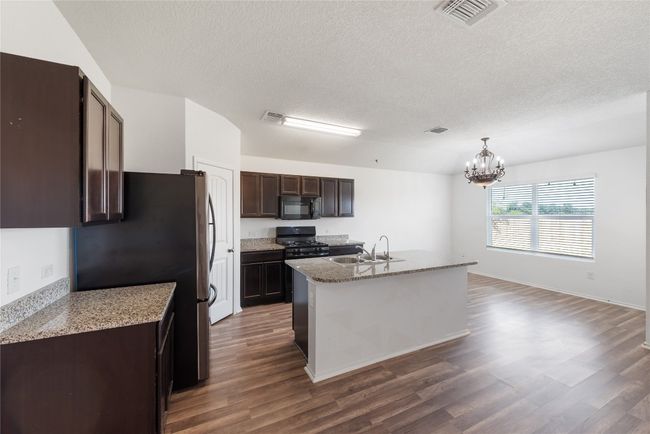 Kitchen featuring a chandelier, dark wood-style floors, a textured ceiling, dark brown cabinetry, and black appliances | Image 6