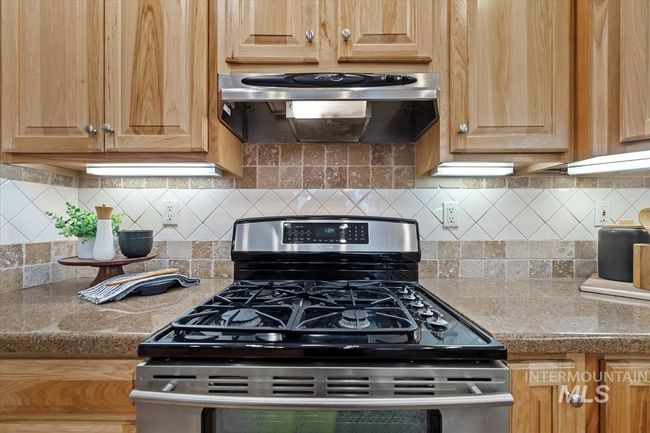 Kitchen with stainless steel gas stove, ventilation hood, tasteful backsplash, light brown cabinets, and light countertops | Image 22
