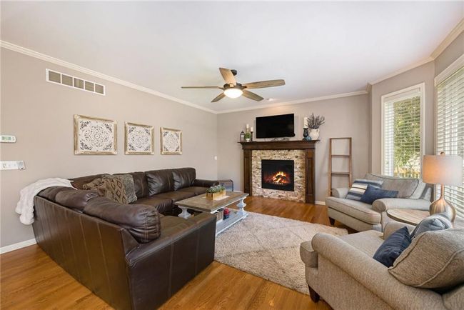 Living area with ceiling fan, ornamental molding, light wood-style flooring, baseboards, and a stone fireplace | Image 9