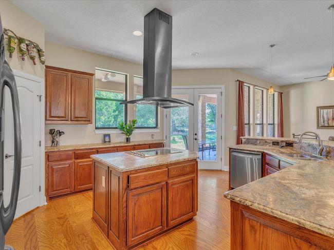 Kitchen with island exhaust hood, black electric stovetop, a kitchen island, stainless steel dishwasher, and a sink | Image 14