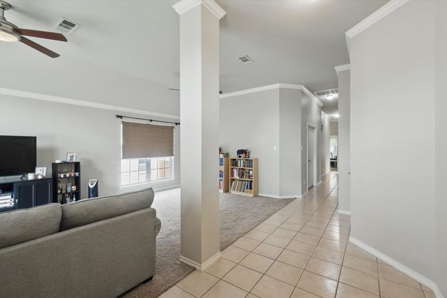 Living room with a ceiling fan, visible vents, crown molding, light tile patterned floors, and light carpet | Image 6