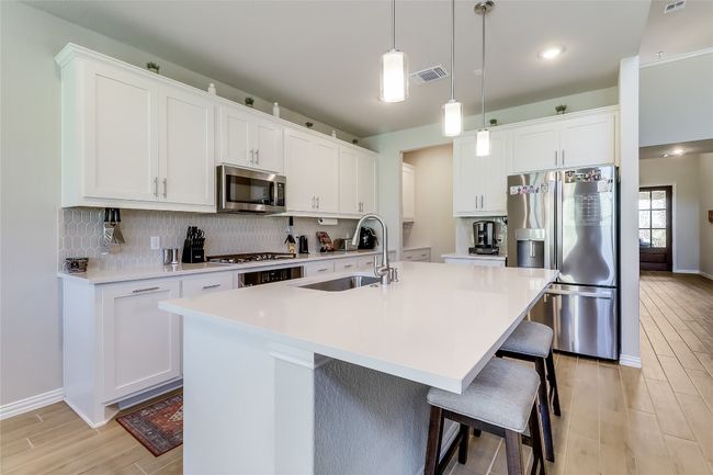 Kitchen featuring appliances with stainless steel finishes, a sink, light wood-style floors, decorative backsplash, and an island with sink | Image 10