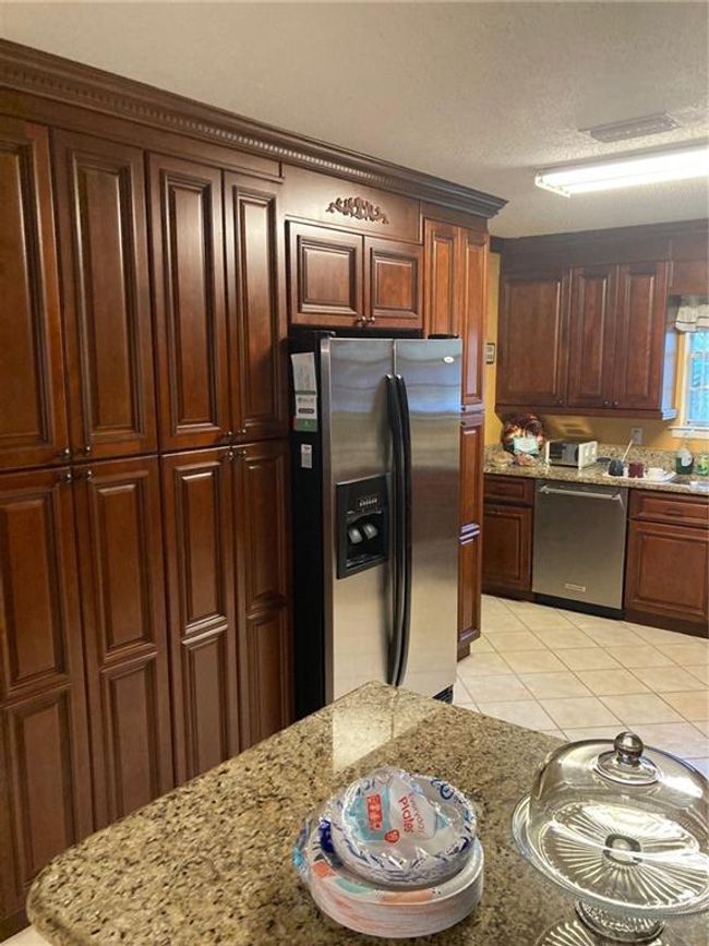 Kitchen with light stone counters, a textured ceiling, light tile patterned floors, stainless steel refrigerator with ice dispenser, and dishwasher | Image 13