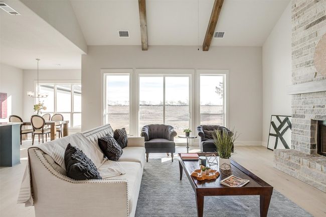 Living room featuring light hardwood / wood-style floors, a notable chandelier, beam ceiling, and a stone fireplace | Image 9