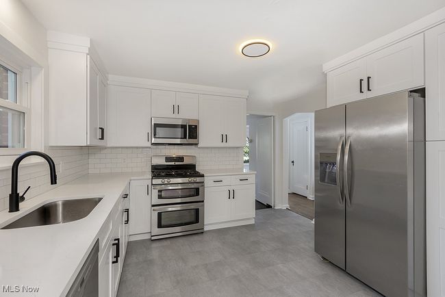 Kitchen with light tile patterned flooring, sink, decorative backsplash, white cabinetry, and stainless steel appliances | Image 17