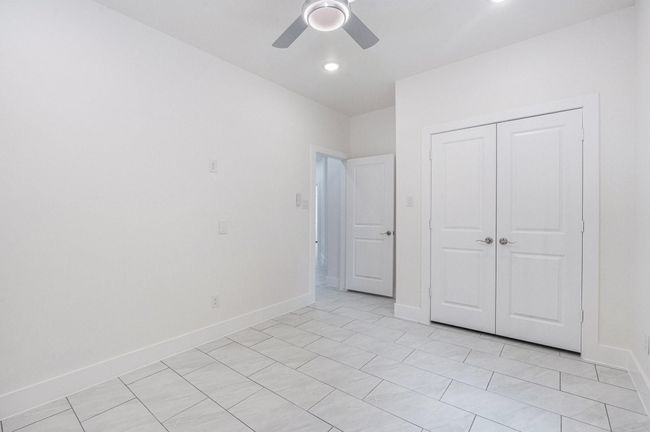 This photo showcases a bright, modern room with tiled flooring, a ceiling fan, and a double-door closet. The neutral color palette and recessed lighting add to the spacious feel, suitable for a bedroom or office. | Image 39