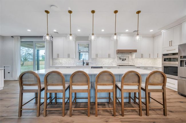 Kitchen with light countertops, white cabinets, custom exhaust hood, appliances with stainless steel finishes, and a spacious island | Image 12
