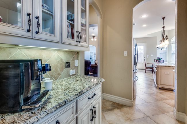 Kitchen featuring decorative backsplash, light stone counters, glass insert cabinets, and arched walkways | Image 19