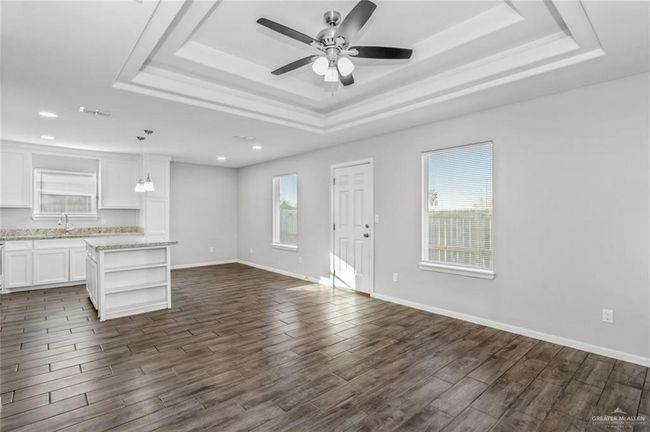 Unfurnished living room featuring a raised ceiling, dark wood finished floors, a sink, ceiling fan, and recessed lighting | Image 4