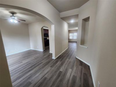 This is a spacious, modern interior featuring an open floor plan with archways, gray wood-like flooring, neutral wall colors, and ample natural light. The living space flows into a well-defined dining area, leading to a kitchen with dark cabinetry. The room includes recessed lighting and a ceiling fan. | Image 3