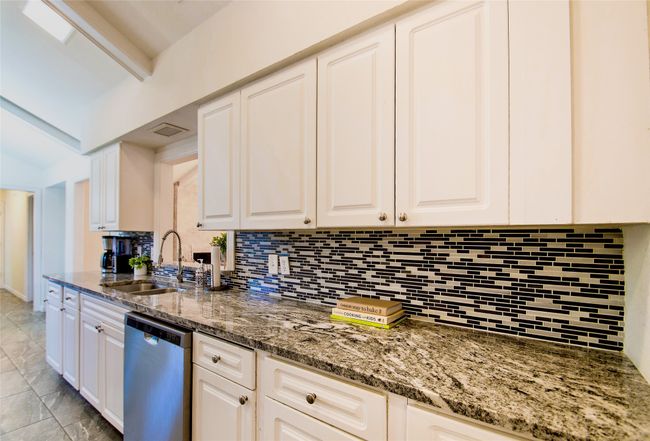 Kitchen with stainless steel dishwasher, backsplash, white cabinets, and stone counters | Image 13