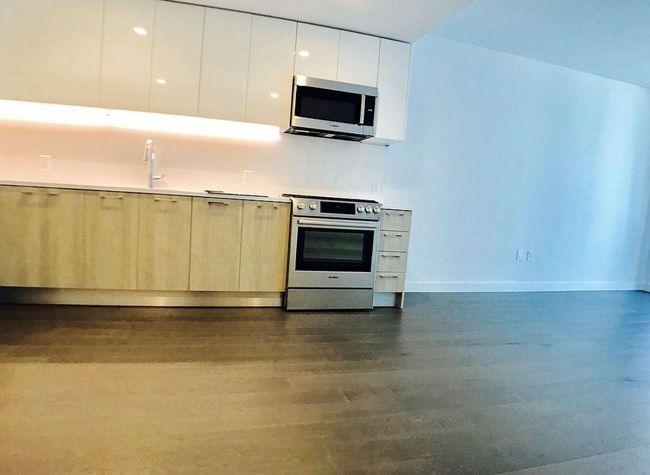 Kitchen with appliances with stainless steel finishes, modern cabinets, dark wood-style flooring, white cabinetry, and light brown cabinets | Image 5