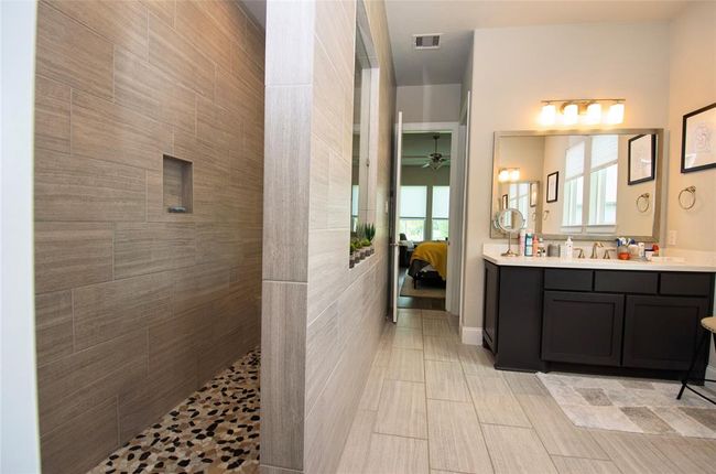 The primary bathroom features a spacious walk-in shower with elegant tile work and pebble flooring. It also includes a double vanities. | Image 16