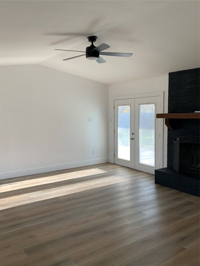 Unfurnished living room with a ceiling fan, vaulted ceiling, wood finished floors, a brick fireplace, and french doors | Image 24