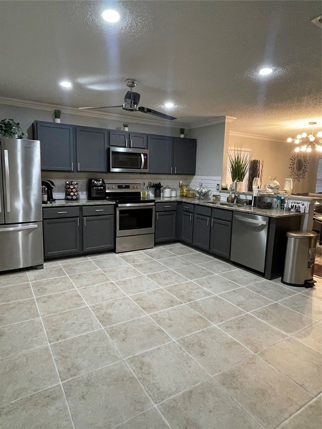 Kitchen with range, refrigerator, dishwashing machine, crown molding, and gray cabinetry | Image 12