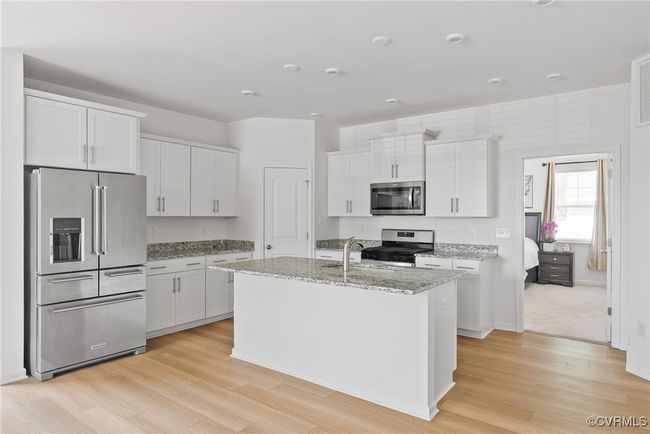Kitchen with white cabinets, stainless steel appliances, light stone counters, and light wood finished floors | Image 11