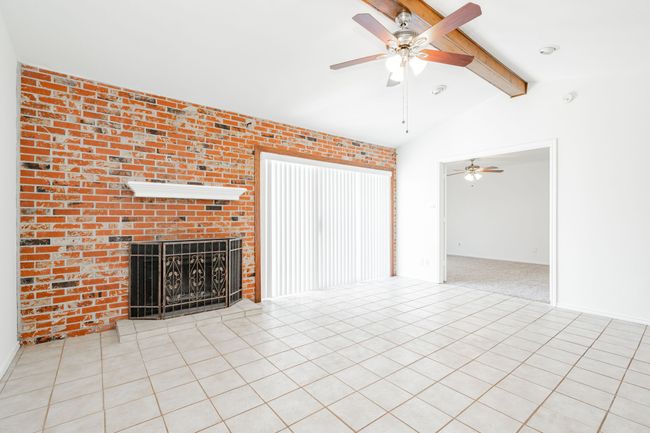 Unfurnished living room featuring a fireplace, lofted ceiling with beams, tile patterned flooring, and ceiling fan | Image 4