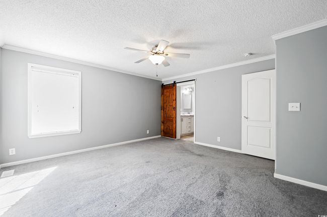 Unfurnished bedroom featuring carpet flooring, a textured ceiling, crown molding, baseboards, and a barn door | Image 19