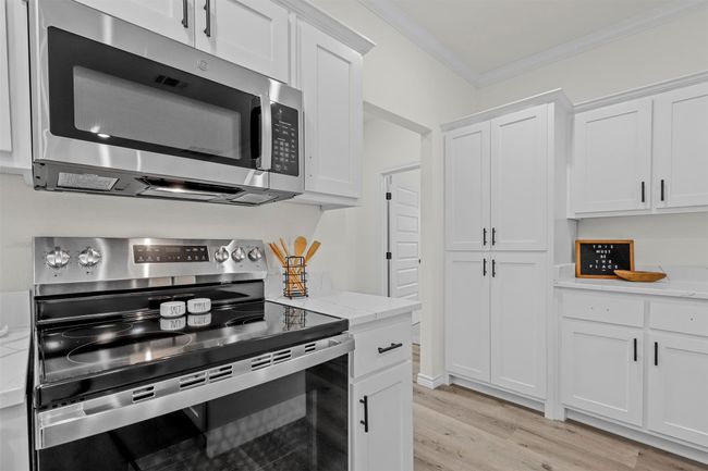 Kitchen featuring stainless steel appliances, light stone countertops, light hardwood / wood-style floors, white cabinets, and crown molding | Image 18