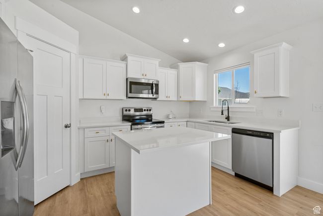 Kitchen featuring stainless steel appliances, white cabinetry, vaulted ceiling, light wood-style flooring, and light countertops | Image 4