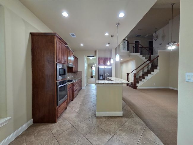 Kitchen featuring stainless steel appliances, light tile patterned flooring, light stone counters, recessed lighting, and open floor plan | Image 12
