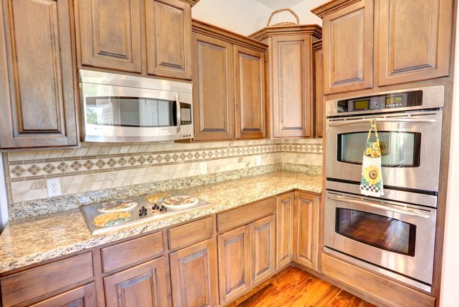 Kitchen featuring light stone countertops, tasteful backsplash, light wood-type flooring, and stainless steel appliances | Image 22