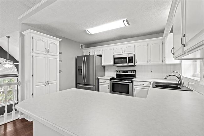 Kitchen with stainless steel appliances, a peninsula, tasteful backsplash, white cabinetry, and light countertops | Image 9
