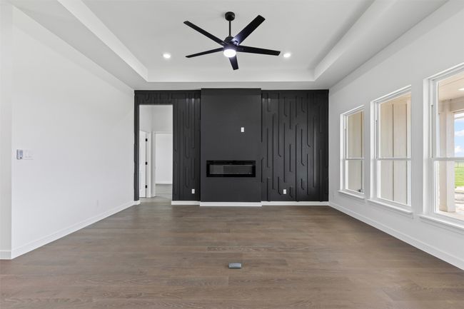 Unfurnished living room with baseboards, ceiling fan, a tray ceiling, and dark wood-style flooring | Image 11