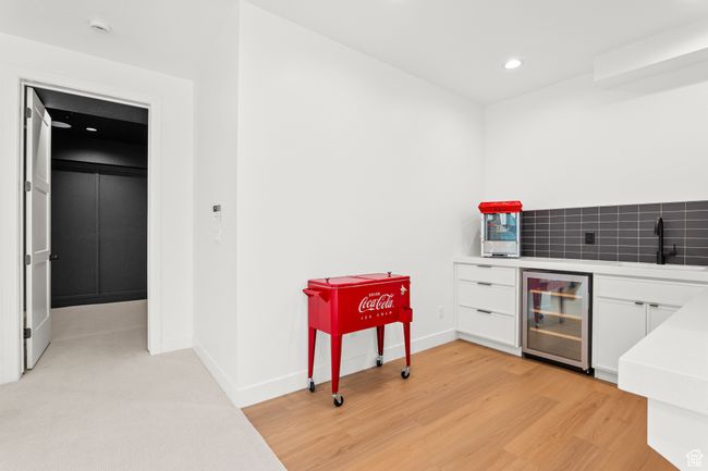 Indoor wet bar featuring recessed lighting, beverage cooler, white cabinets, light wood-type flooring, and light stone counters | Image 54