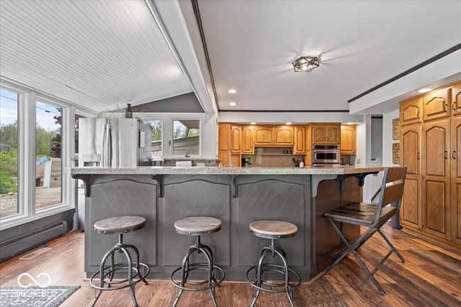 kitchen featuring stainless steel appliances, a baseboard radiator, a kitchen bar, wood finished floors, and lofted ceiling | Image 16