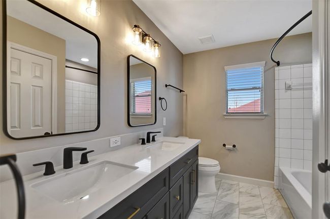 This bathroom features a modern double vanity with matte black fixtures, large framed mirrors, and elegant lighting. The room includes a shower-tub combo with white tile and a window for natural light, complemented by stylish marble-patterned flooring. | Image 40