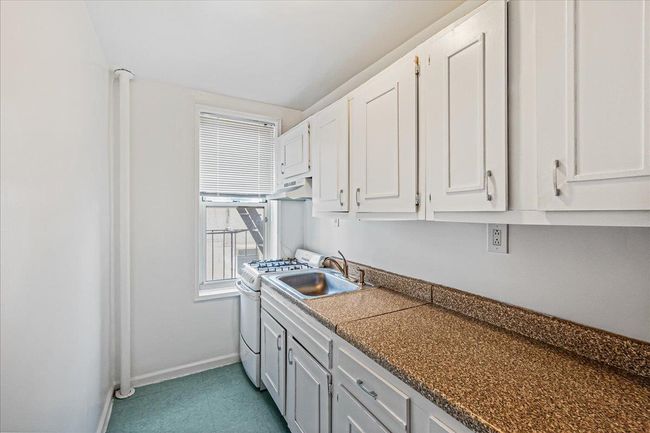 Kitchen with white range with gas cooktop, white cabinetry, under cabinet range hood, and dark countertops | Image 5
