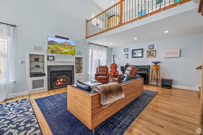 Living room featuring recessed lighting, a towering ceiling, light wood-style flooring, a glass covered fireplace, and baseboards | Image 20