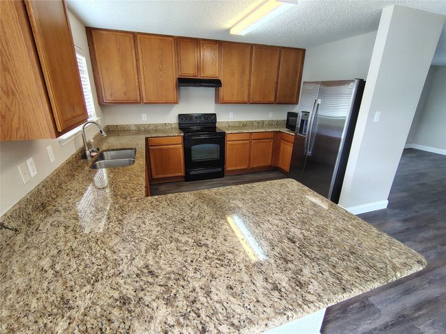 Kitchen with black appliances, a sink, brown cabinetry, under cabinet range hood, and a peninsula | Image 18