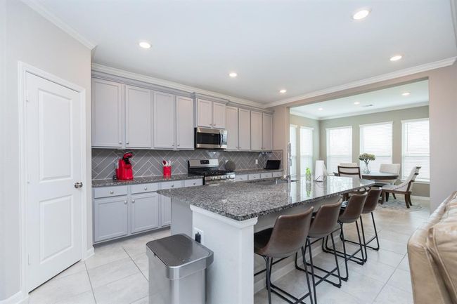 kitchen features gray cabinetry, a large granite island with seating, stainless steel appliances, and an open layout that flows into a breakfast area. | Image 11