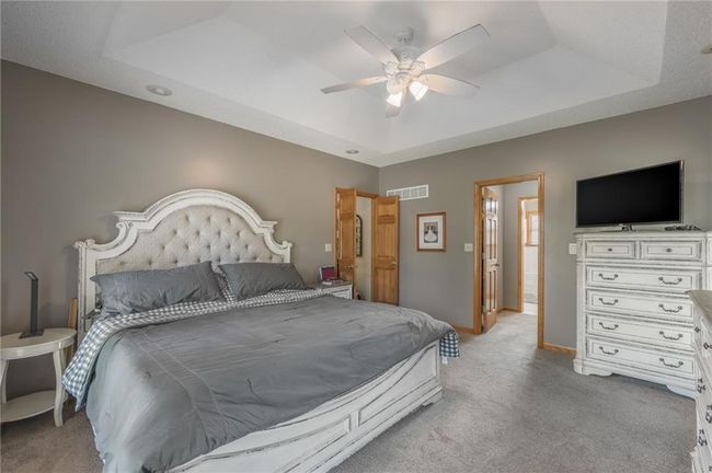 Bedroom with a ceiling fan, a tray ceiling, baseboards, visible vents, and light carpet | Image 46