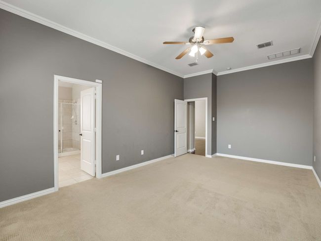 Unfurnished bedroom featuring ornamental molding, light colored carpet, ensuite bath, and a ceiling fan | Image 24