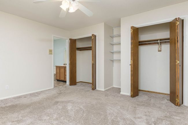 Unfurnished bedroom featuring light colored carpet, multiple closets, ceiling fan, and ensuite bathroom | Image 9
