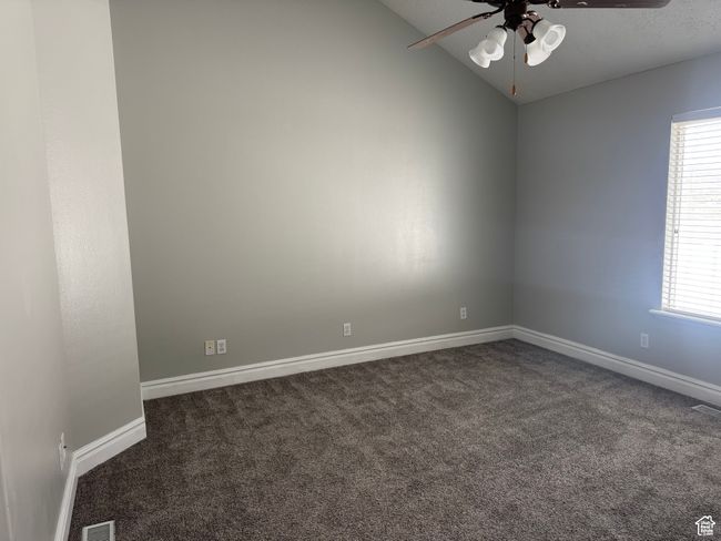 Unfurnished room with a ceiling fan, dark carpet, lofted ceiling, plenty of natural light, and baseboards | Image 9