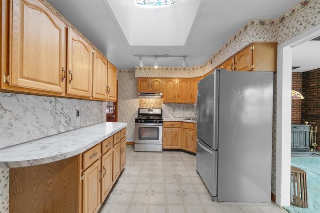 Kitchen with wallpapered walls, appliances with stainless steel finishes, light floors, light countertops, and under cabinet range hood | Image 11
