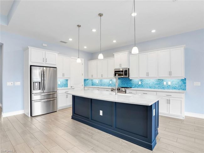 Kitchen featuring appliances with stainless steel finishes, decorative light fixtures, white cabinetry, and an island with sink | Image 12