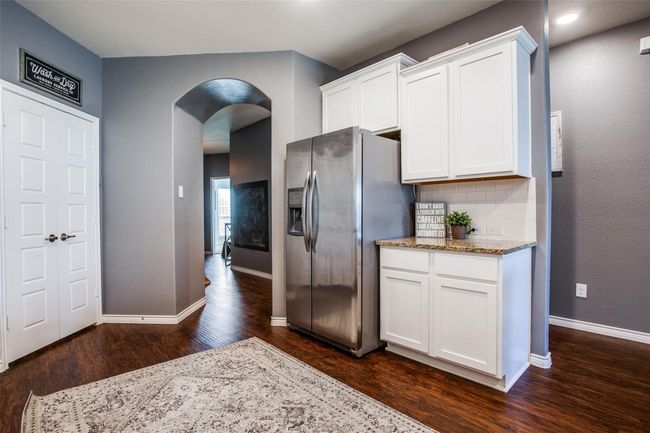 Kitchen with backsplash, dark hardwood / wood-style flooring, white cabinets, and stainless steel fridge | Image 11