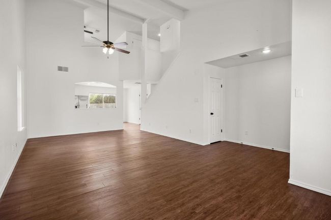 Unfurnished living room featuring a high ceiling, a ceiling fan, dark wood-type flooring, and visible vents | Image 4
