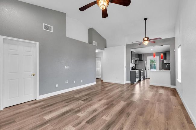 Unfurnished living room with a ceiling fan, high vaulted ceiling, wood finished floors, baseboards, and a sink | Image 7