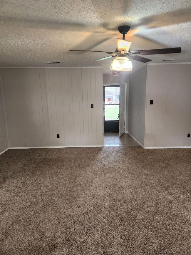Carpeted empty room with ceiling fan, a textured ceiling, and wood walls | Image 13