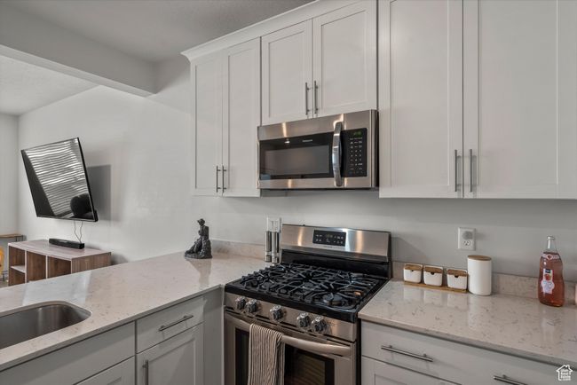 Kitchen with stainless steel appliances, white cabinetry, and light stone countertops | Image 10